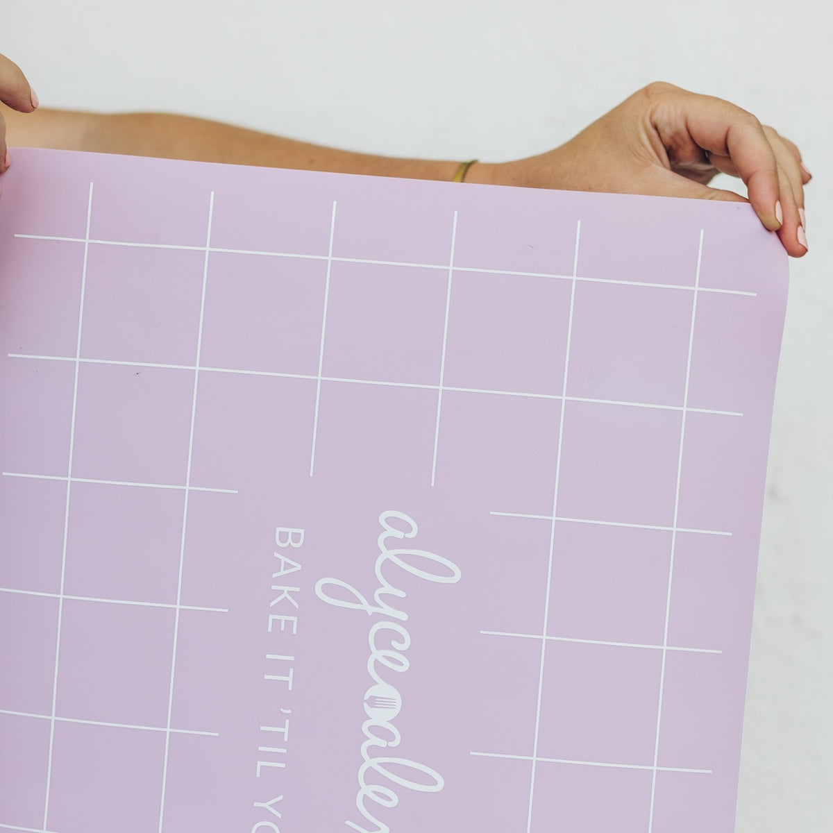 Hands unrolling the lilac Silicone Baking Mat to show its flexibility