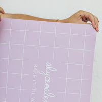 Hands unrolling the lilac Silicone Baking Mat to show its flexibility