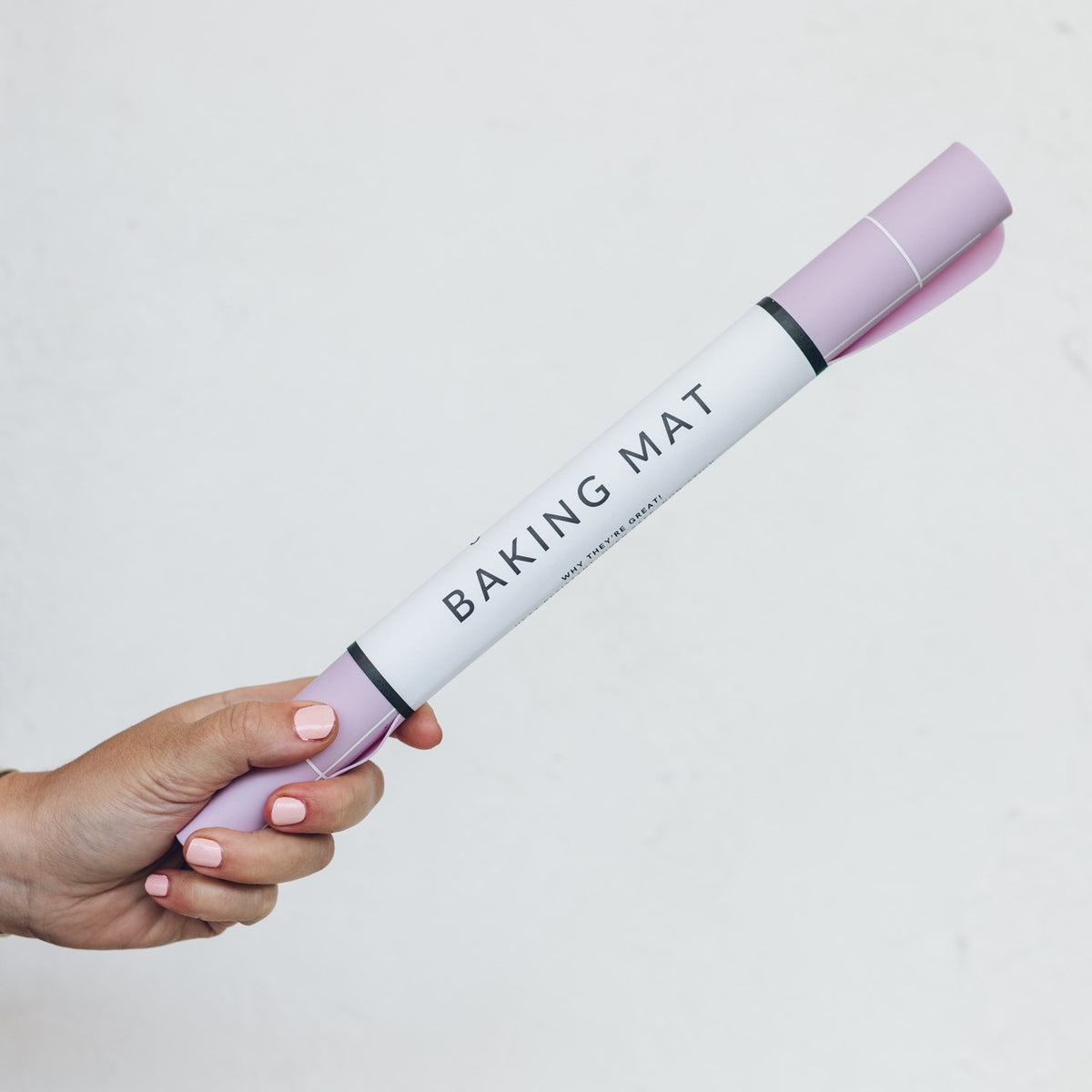 Hand holding a rolled lilac Silicone Baking Mat in its tube