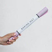 Hand holding a rolled lilac Silicone Baking Mat in its tube