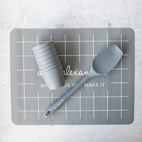Grey Silicone Baking Mat with a cup, spatula and measuring tools arranged on it
