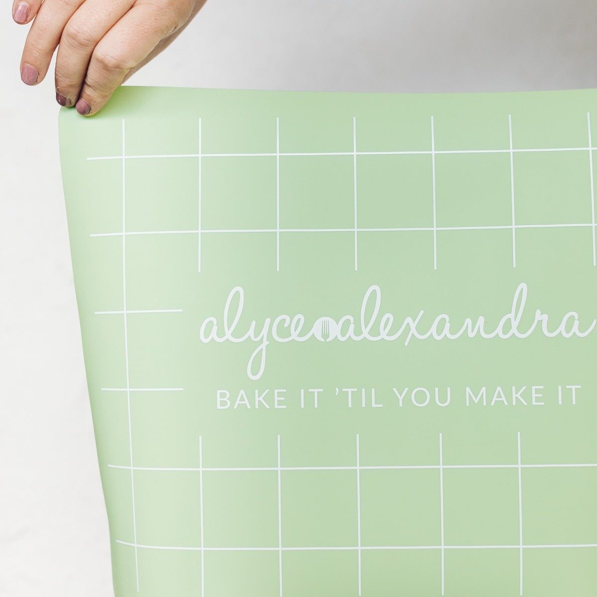 Hand unrolling the sage green Silicone Baking Mat, showing the grid guide