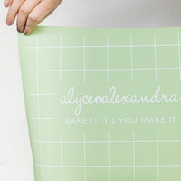 Hand unrolling the sage green Silicone Baking Mat, showing the grid guide