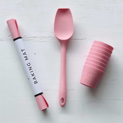 Rolled Silicone Baking Mat in its tube beside a pink spatula and stacked pink cups