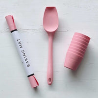 Rolled Silicone Baking Mat in its tube beside a pink spatula and stacked pink cups