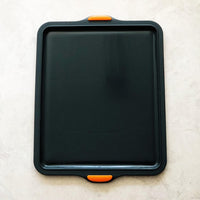 Silicone Baking Tray in charcoal with orange silicone handles, shown from above