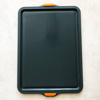 Silicone Baking Tray shown from above, its non-stick surface and orange grips visible
