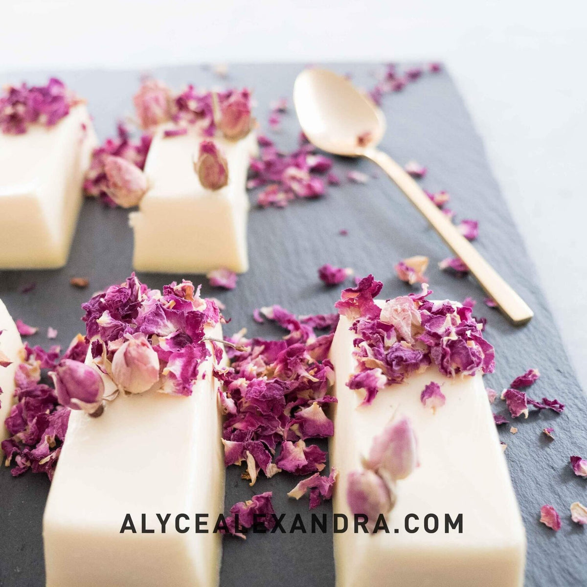 White chocolate bars topped with dried rose petals on slate with a gold spoon, made in the Silicone Bar Moulds
