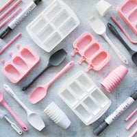 Flat lay of the alyce alexandra silicone range in pink, white and grey, including dariole moulds and spatulas