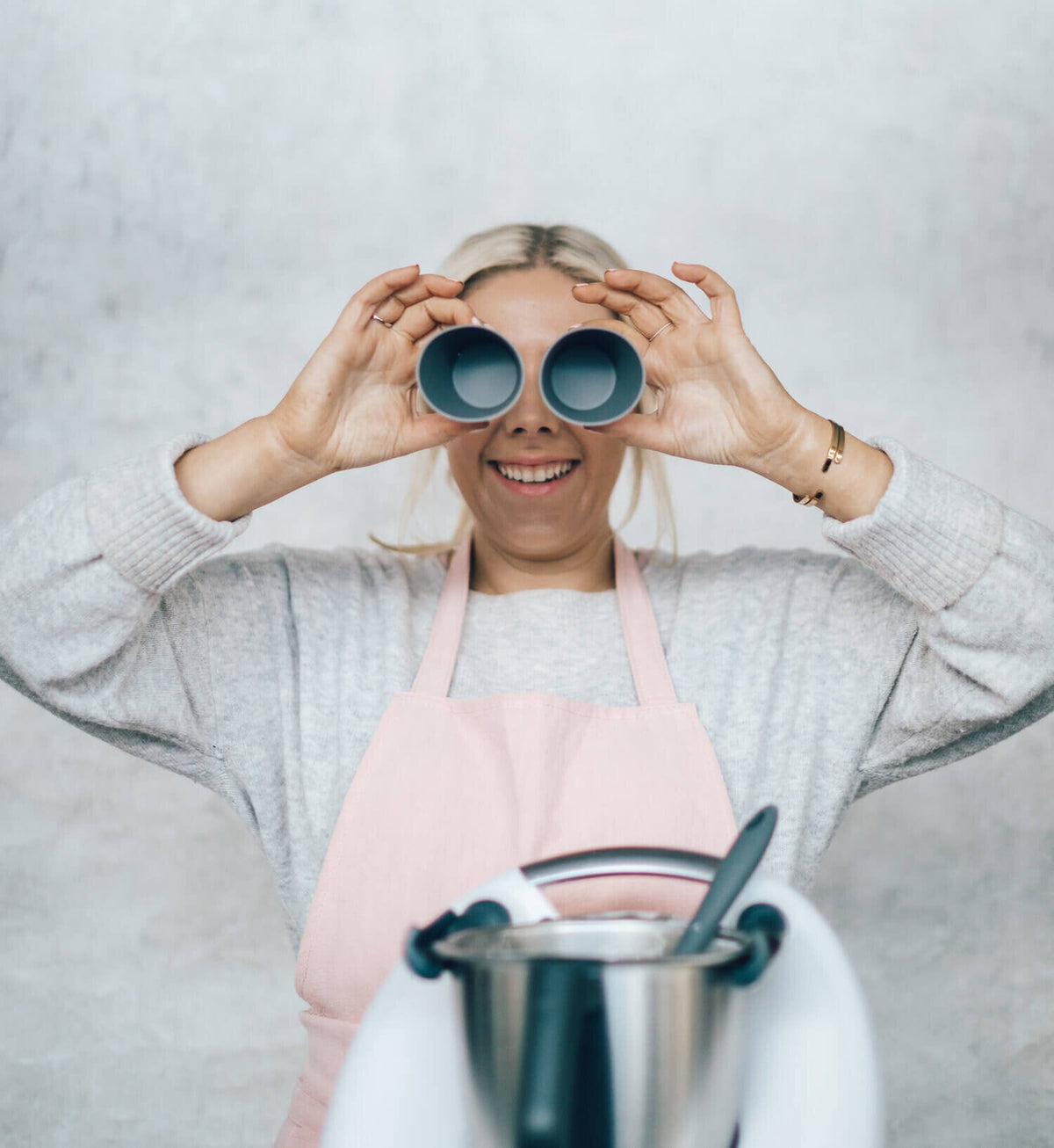 Woman holding two Silicone Dariole Moulds up to her eyes like binoculars beside a Thermomix