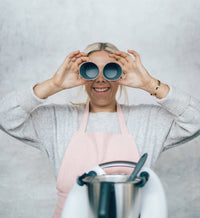 Woman holding two Silicone Dariole Moulds up to her eyes like binoculars beside a Thermomix