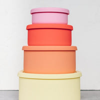 Four Silicone Nesting Bowls stacked in yellow, peach, red and pink with their lids on