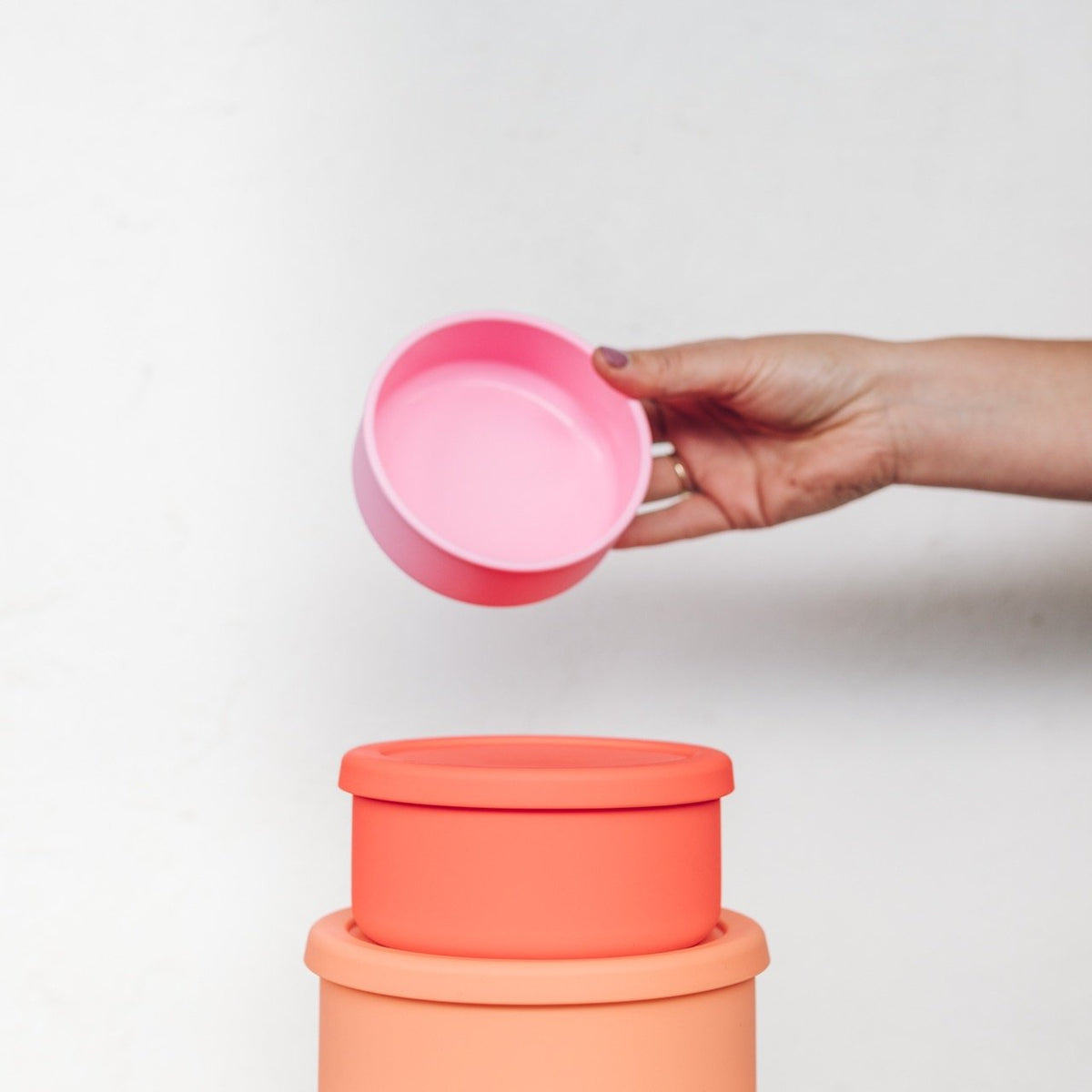 Hand lifting the pink lid off a Silicone Nesting Bowl