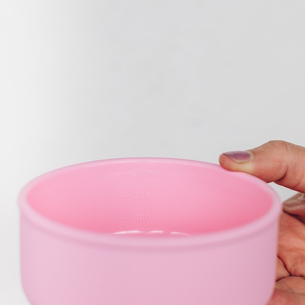 Hand holding the pink Silicone Nesting Bowl to show its flexible sides