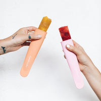Two Silicone Push Up Ice Cream Moulds filled with mango and berry ice blocks, pushed part way up