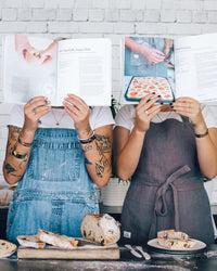 Two people in aprons holding Simple Sourdough open in front of their faces