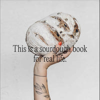 Hand holding up a round sourdough loaf of bread; this is a sourdough book for real life