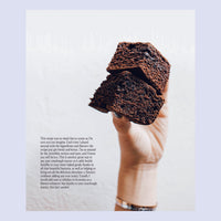 Hand holding a slice of dark chocolate sourdough loaf of bread