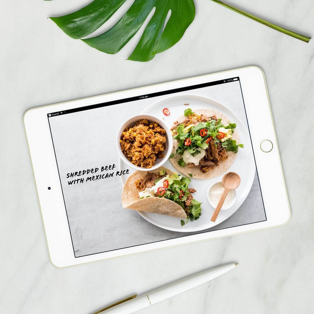Shredded beef with Mexican rice shown on a tablet beside a monstera leaf