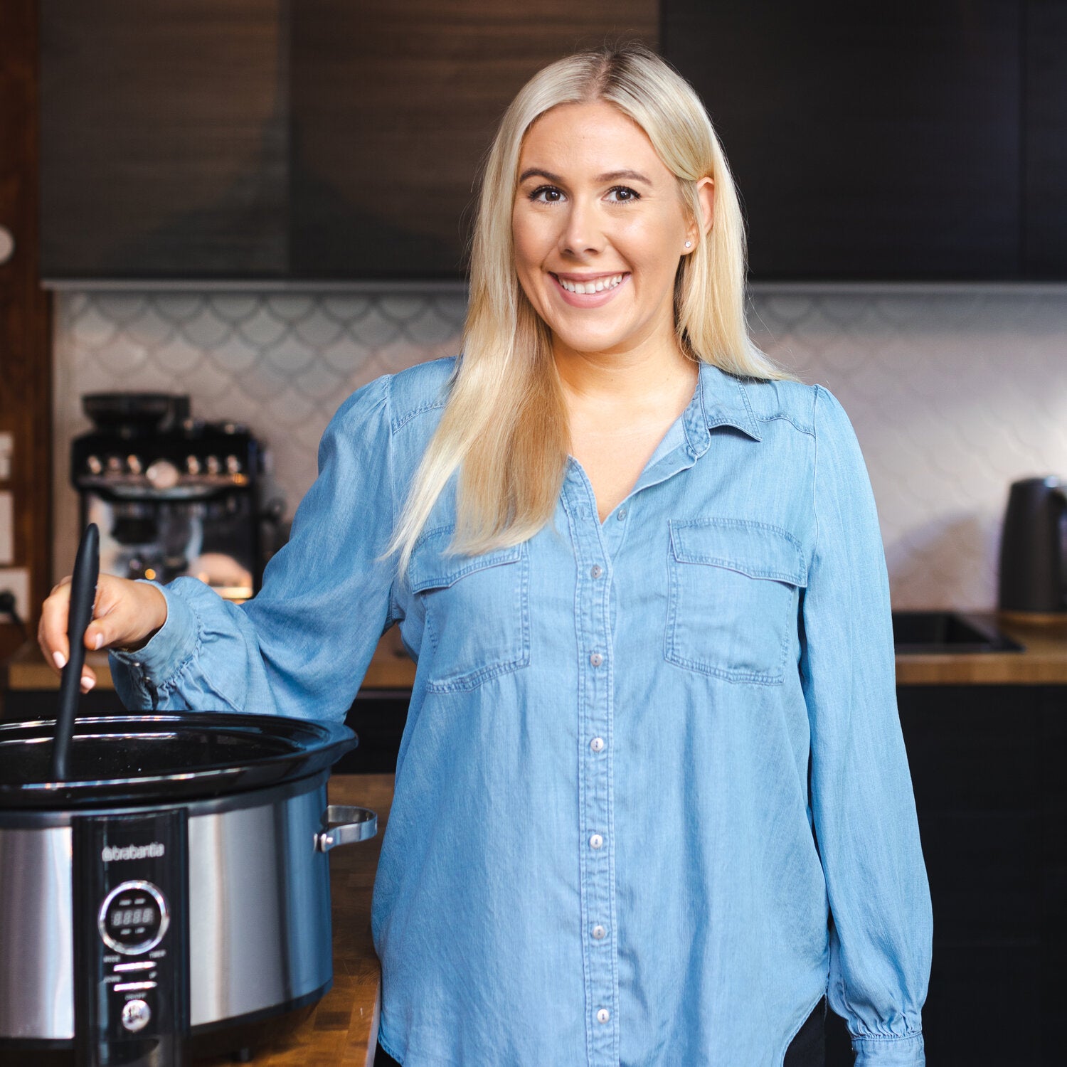 Alyce standing beside her slow cooker in the kitchen holding a Slow Cooker Spatula