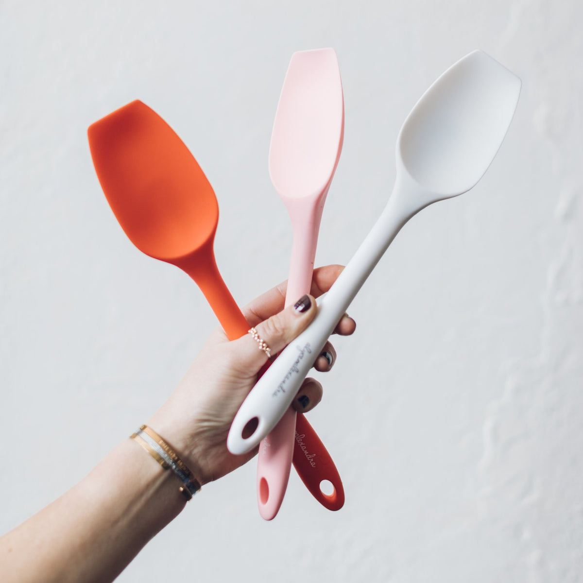 Hand holding orange, pink and white Slow Cooker Spatulas together
