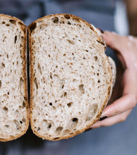 Hands holding a sourdough loaf of bread cut in half to show its open crumb