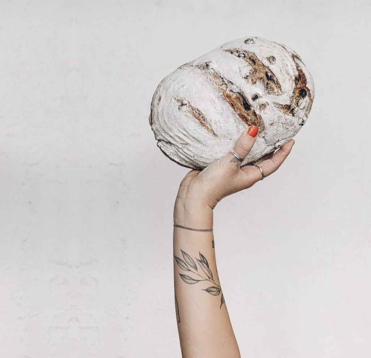 Hand holding up a round sourdough loaf of bread dusted with flour