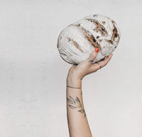 Hand holding up a round sourdough loaf of bread dusted with flour