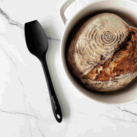 Black Sourdough Spatula beside a baked sourdough loaf of bread in a pot