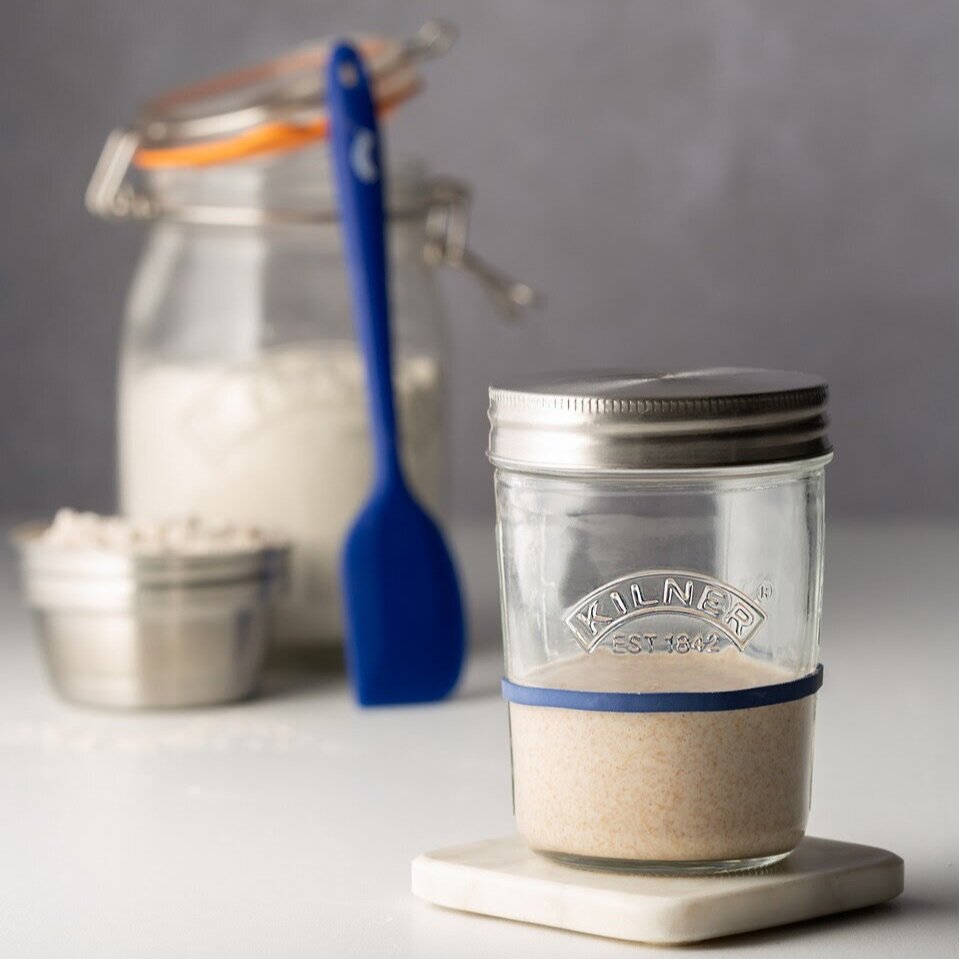 Kilner glass sourdough starter jar with a blue silicone spatula and a jar of flour alongside