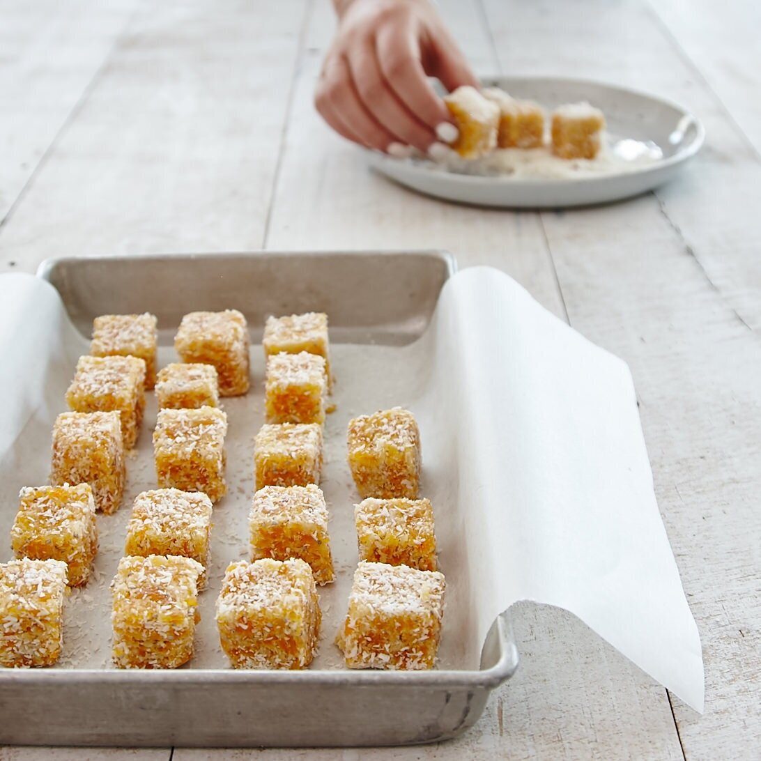 Tray of coconut-coated lamingtons being lifted out on baking paper, made using the Starter Kit