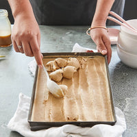 Hands lifting shaped dough from a tray, made using the Starter Kit