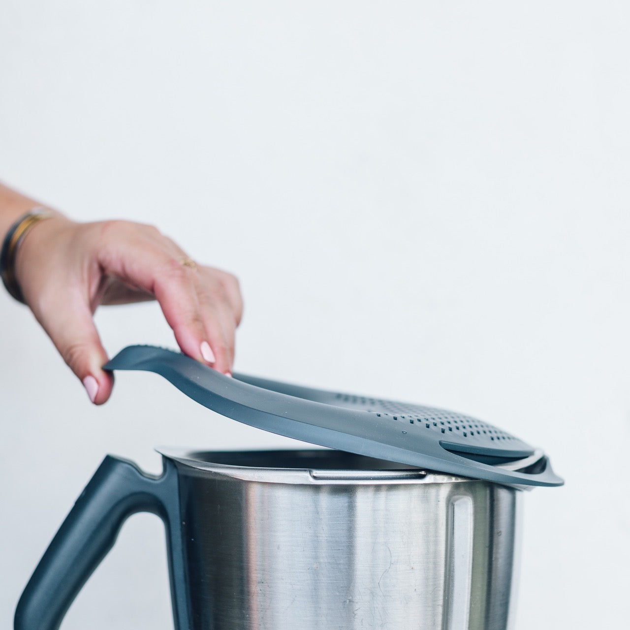 Hands fitting the Thermo Lid Strainer onto the rim of a Thermomix mixing bowl
