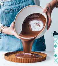 Hands pouring chocolate ganache into a tart shell, from Thermo Plant-Based