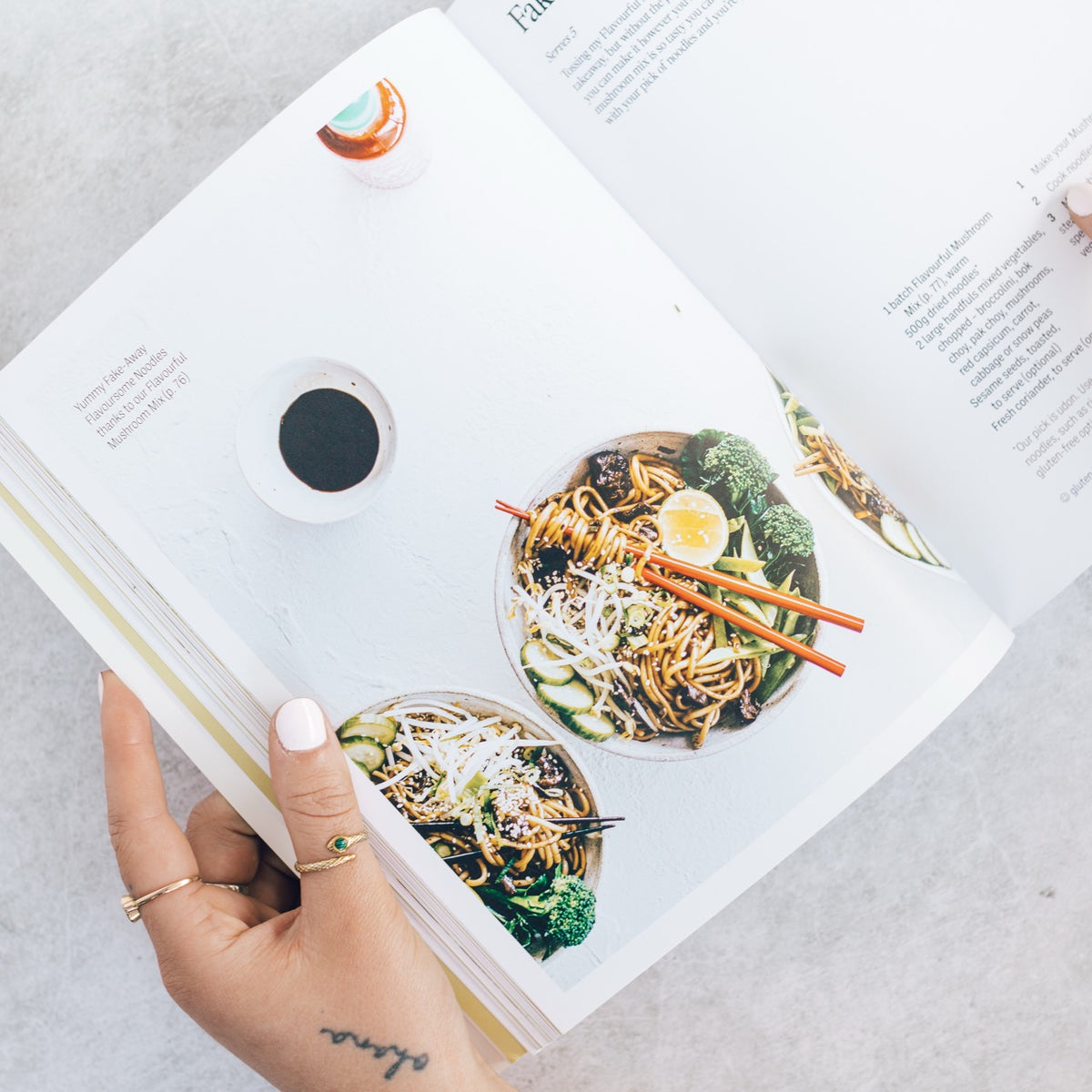 Hands holding Thermo Plant-Based open at a noodle salad recipe beside a coffee