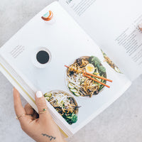 Hands holding Thermo Plant-Based open at a noodle salad recipe beside a coffee