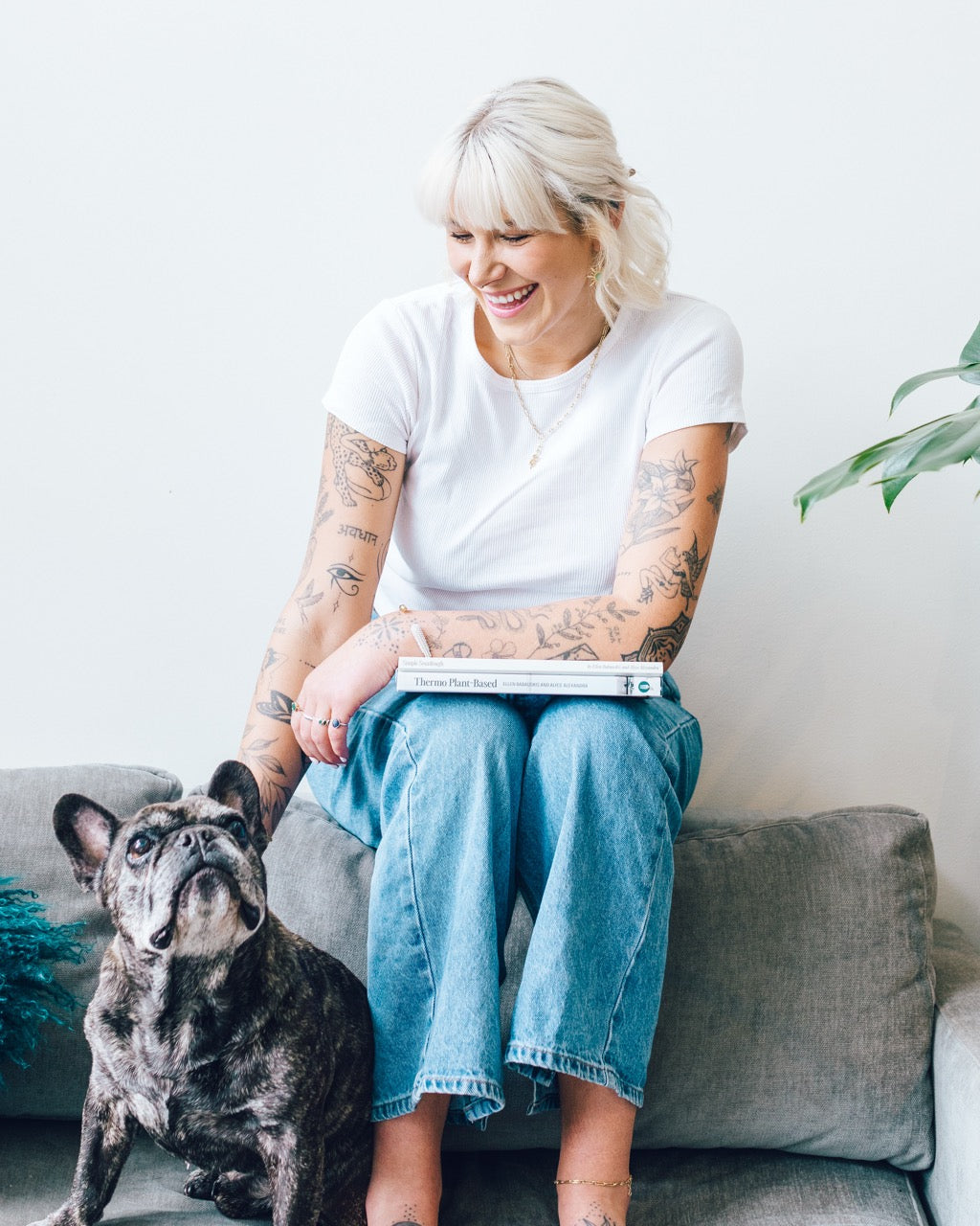 Woman sitting on a sofa reading Thermo Plant-Based with a french bulldog beside her