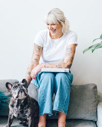 Woman sitting on a sofa reading Thermo Plant-Based with a french bulldog beside her