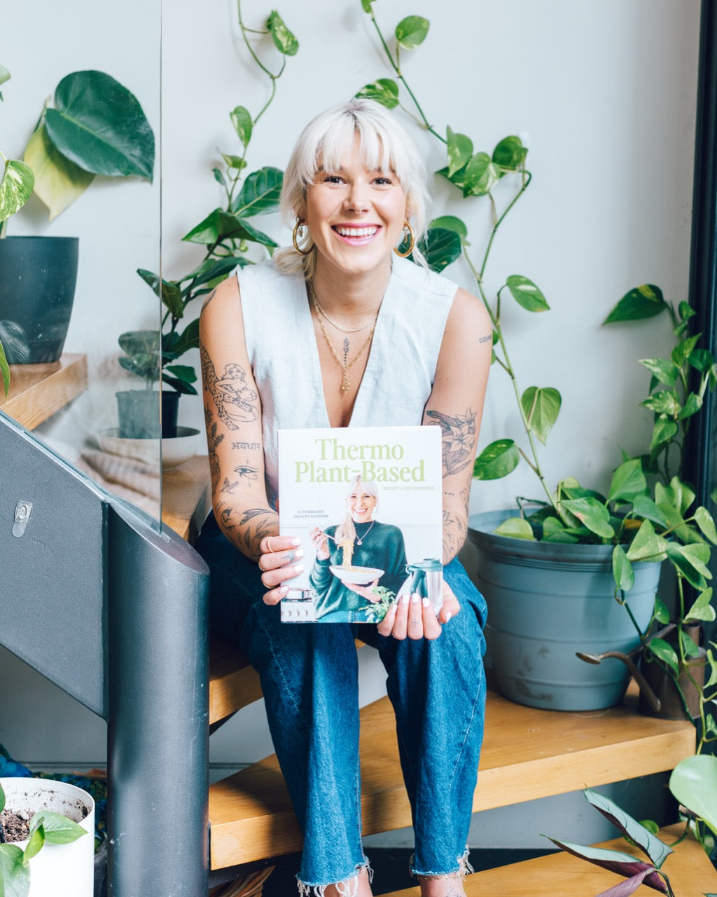 Woman holding a copy of Thermo Plant-Based in a room filled with plants