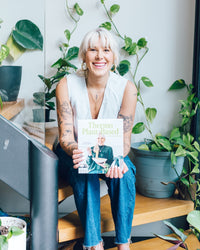 Woman holding a copy of Thermo Plant-Based in a room filled with plants