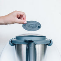 Thermo Splash Cap held above the Thermomix bowl, ready to fit