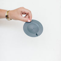 Hand holding the Thermo Splash Cap by its edge against a pale background