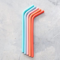 Four Wide Reusable Silicone Straws in teal, pink, coral and blue laid on a grey surface