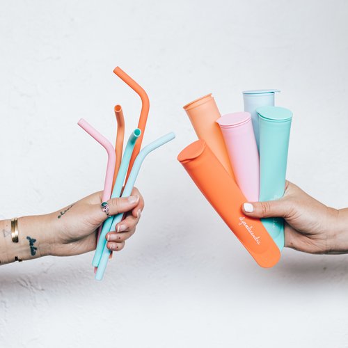 Hands holding Wide Reusable Silicone Straws in several colours beside matching cups