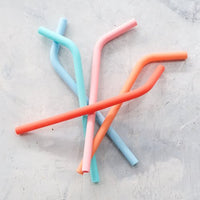 Wide Reusable Silicone Straws in mixed colours scattered on a grey surface