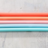Wide Reusable Silicone Straws in coral, pink and blue laid across a pale surface