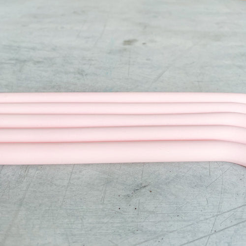 Four pink Wide Reusable Silicone Straws laid parallel on a grey surface, showing their bend