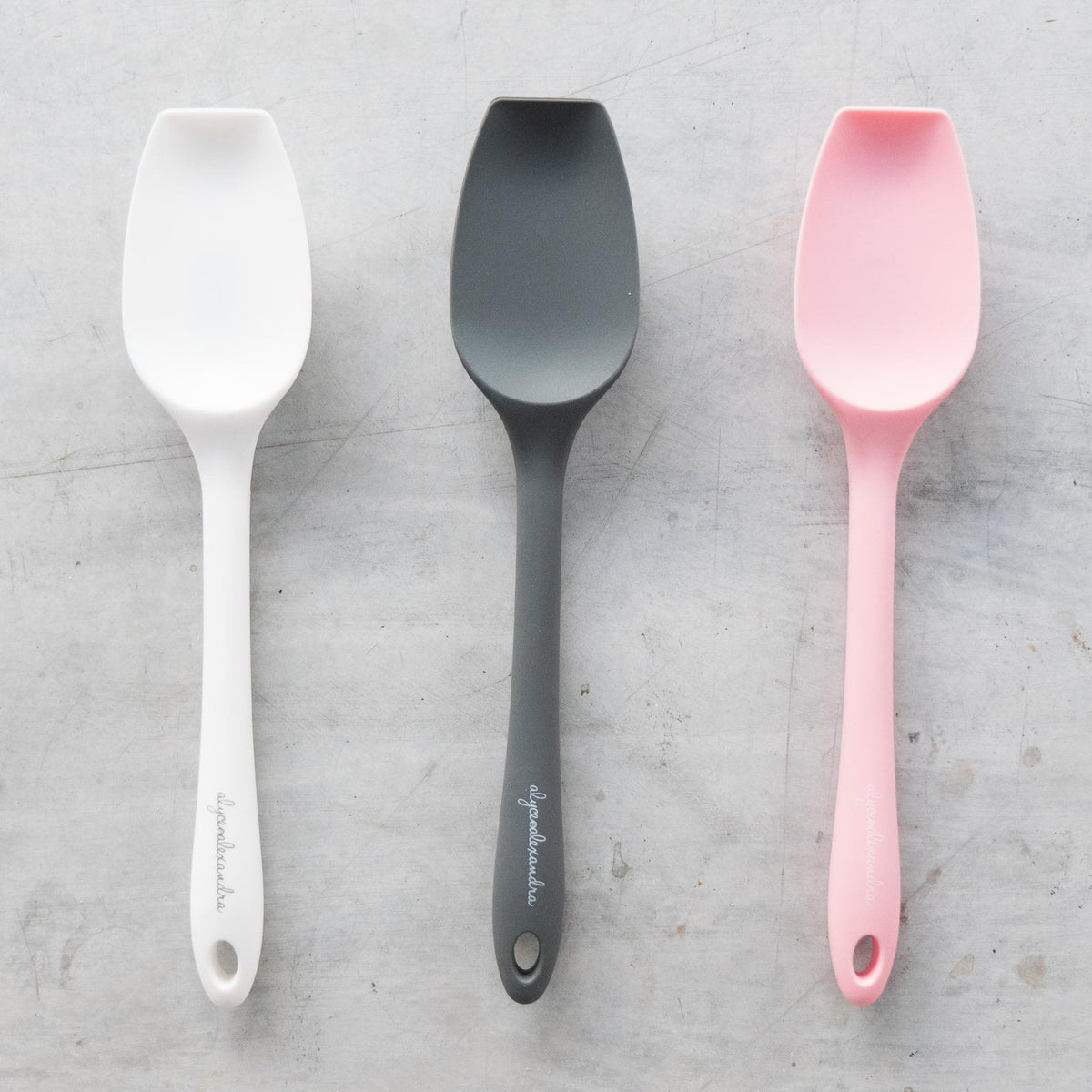Three Slow Cooker Spatulas laid side by side in cream, charcoal and pink