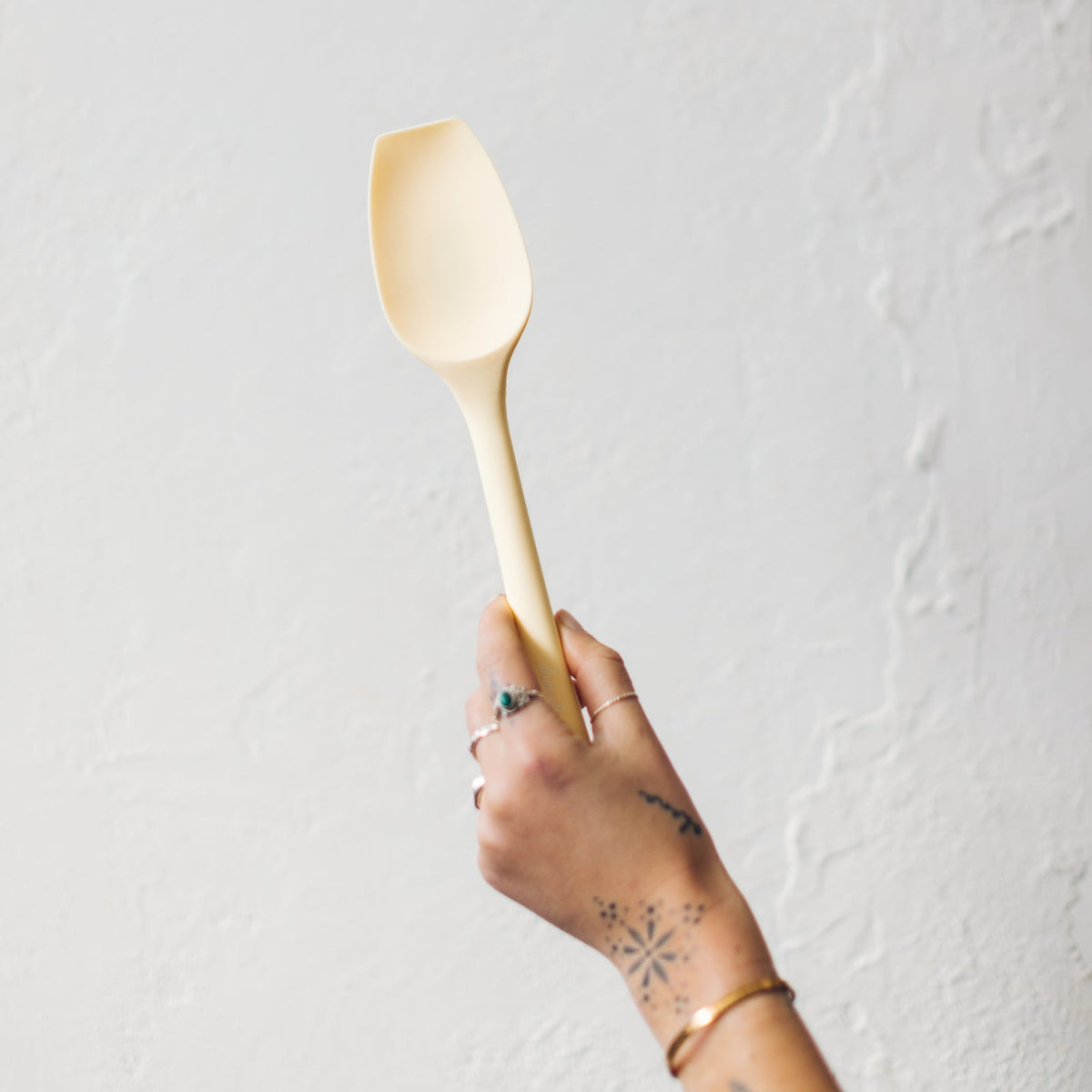 Hand holding a cream Slow Cooker Spatula against a pale background
